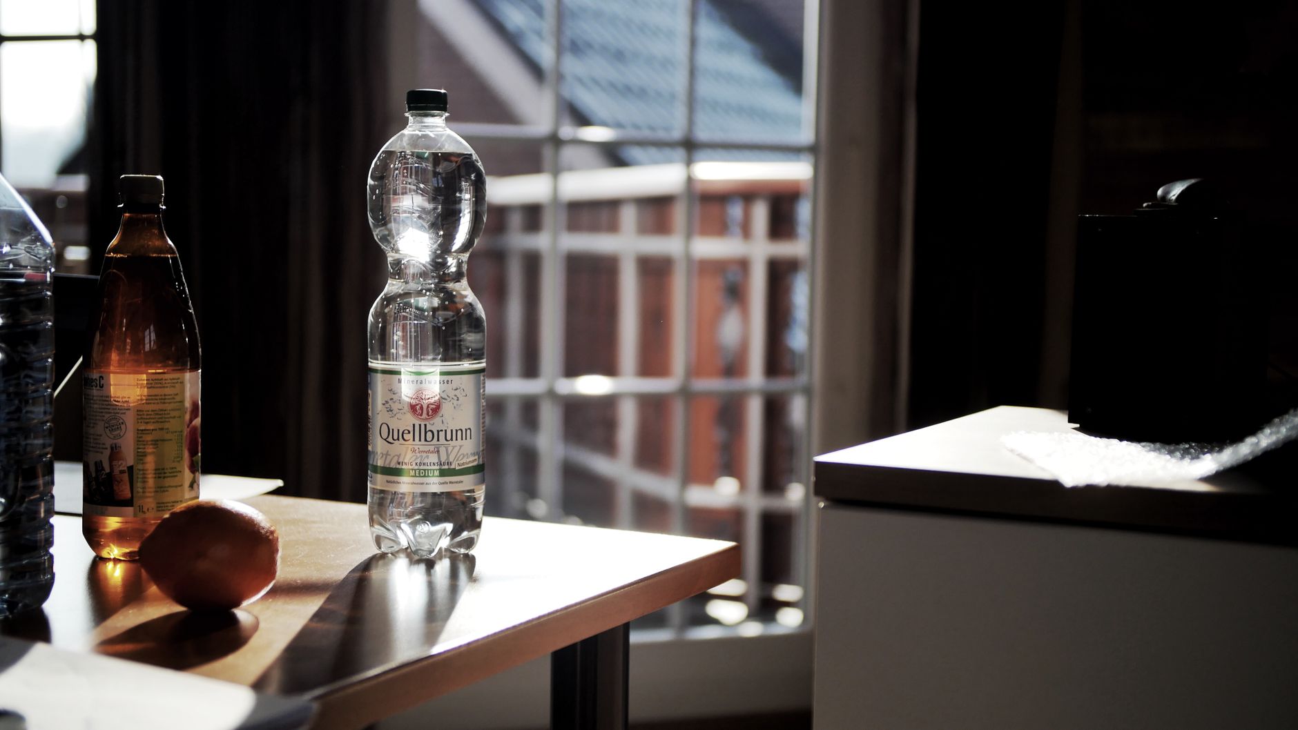 Verre d'eau rempli au robinet à côté d'une carafe filtrante et d'une gourde en verre sur un plan de travail en bois